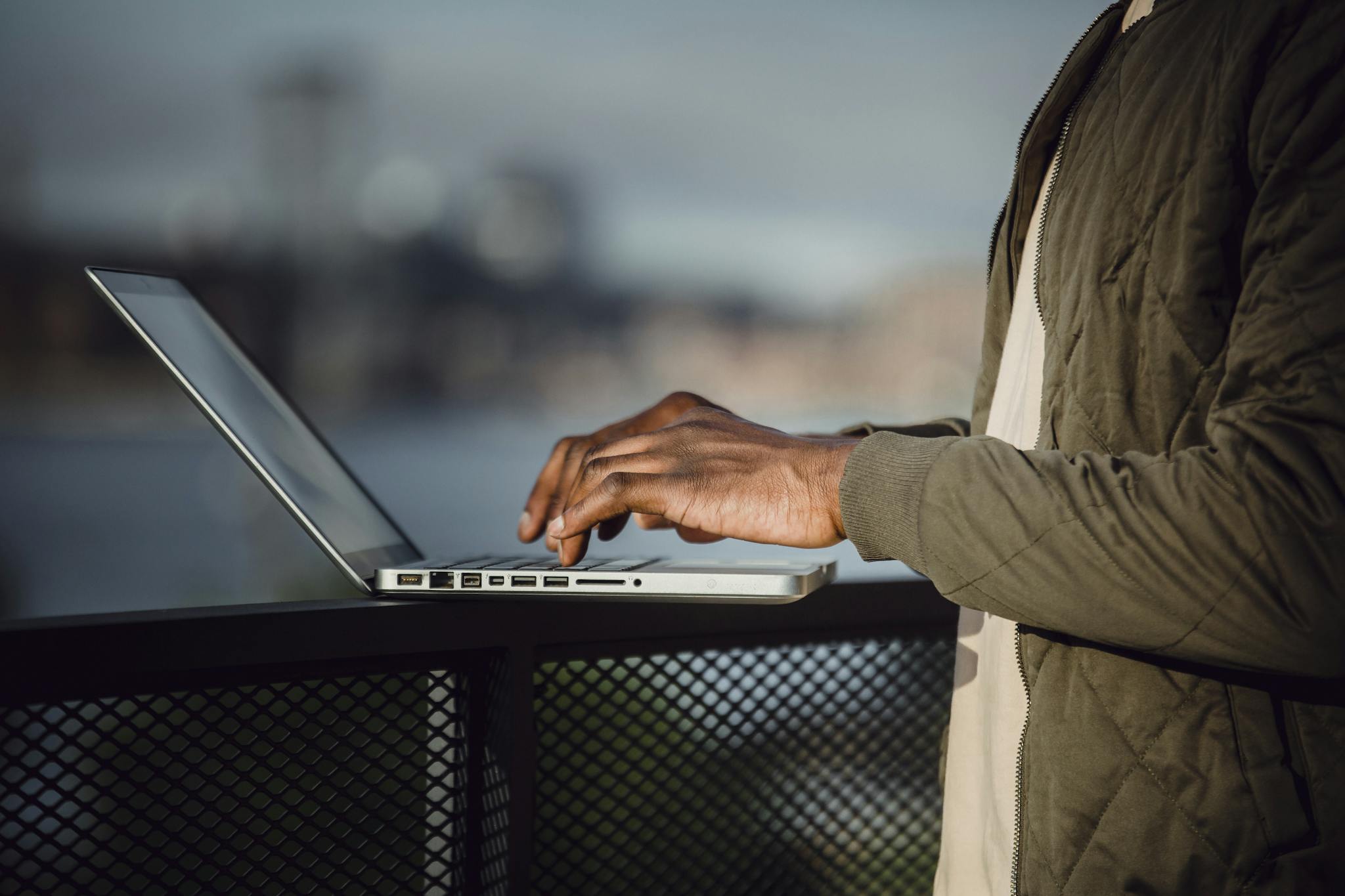 Man working on a laptop outdoors with city skyline background.